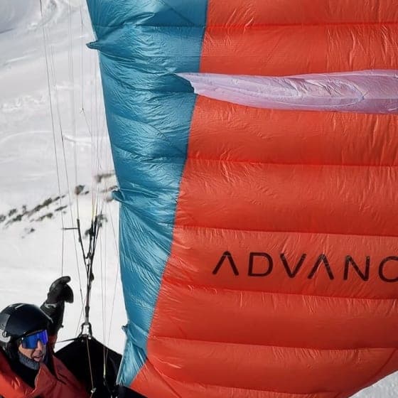 Pilot unter einem grossen roten Gleitschirm auf einem verschneiten Startplatz