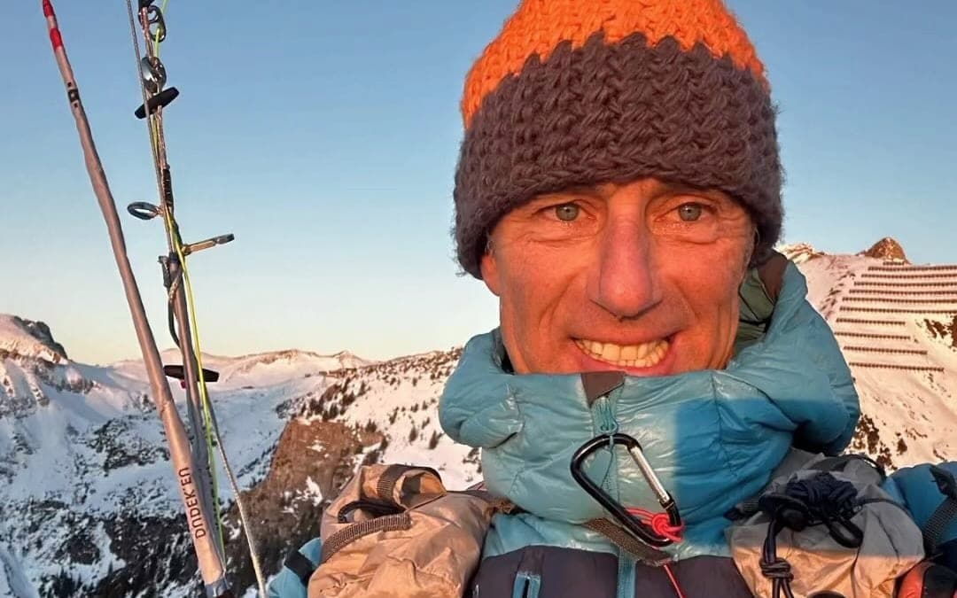 Robert Blum mit Mütze und Flugausrüstung auf einem verschneiten Grat im Abendlicht
