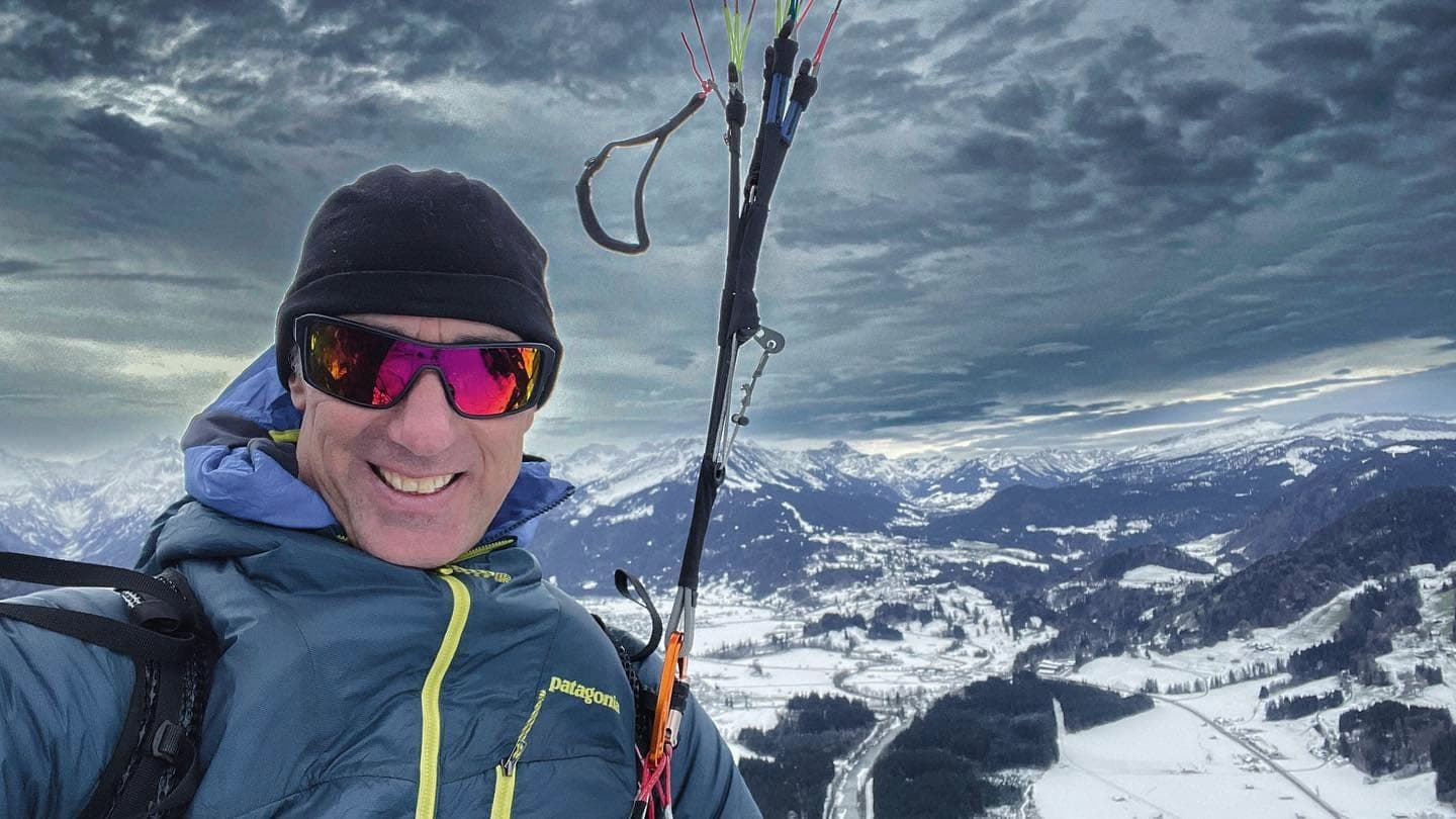 Robert Blum im Gurtzeug während des Fluges, hinter ihm das verschneite Oberallgäu