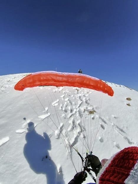 Aufgezogener Gleitschirm auf einem verschneiten Startplatz, der Schatten des Piloten davor