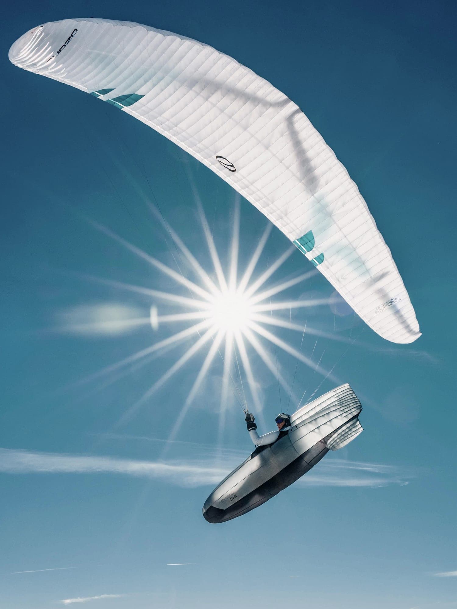 Gleitschirm im Gegenlicht hoch über einer verschneiten Bergkette, die Sonne als Stern hinter dem Schirm