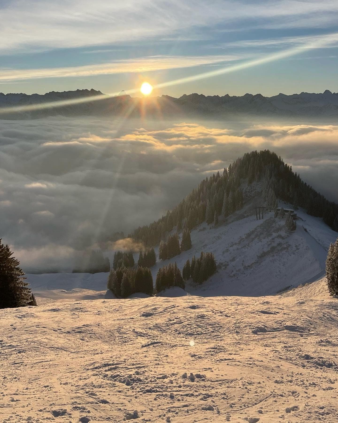 Sonnenaufgang über einem geschlossenen Nebelmeer, ein bewaldeter Grat ragt heraus